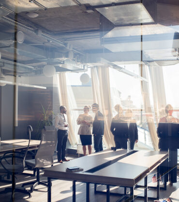 Wide angle view of group of successful businespeople discussing projects behind glass wall in office, copy space