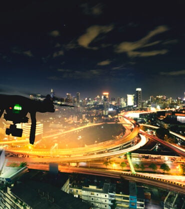 Drone (Multi-rotor) silhouette flying above the city panorama at night scene.