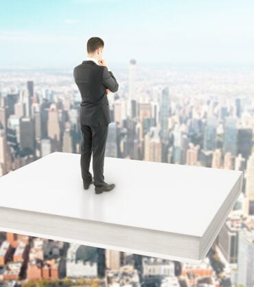Businessman standing on a white book soaring over city