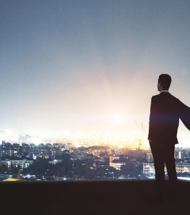 Young backlit super hero businessman on rooftop with night city view. Leadership and success concept