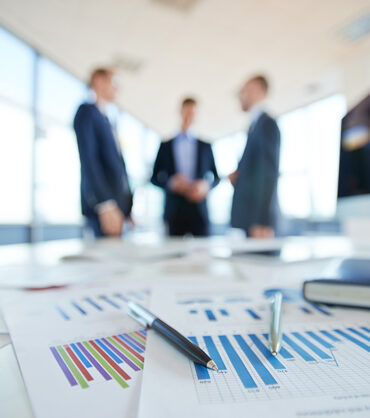 Documents on office table and three men talking in the background