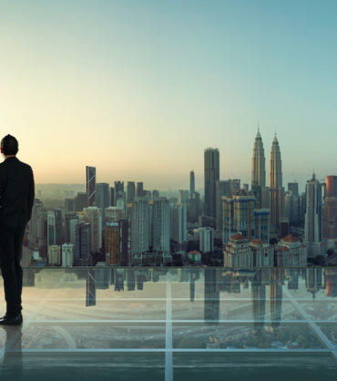 Businessman standing at transparent glass floor on rooftop with city skyline, success and thinking concept  .