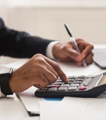 Accounting consulting concept. Businessman checking on incomes in office, using calculator, taking notes, cropped