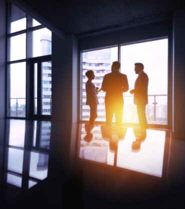 Group of three silhouettes businessmen discussing in office near big window. Business concept