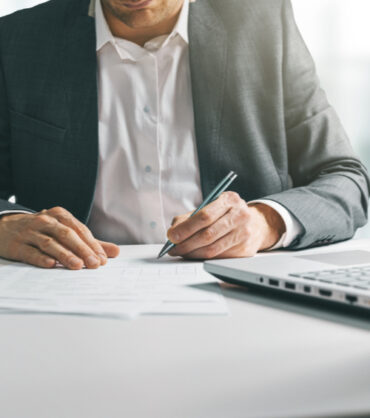 young man in suit writing business papers at desk in modern coworking office. copy space