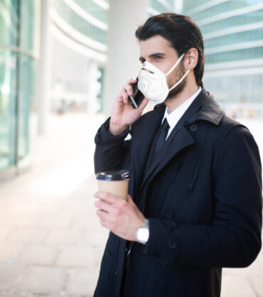 Portrait of a businessman holding a cup of coffee while wearing a mask, coronavirus pandemic concept
