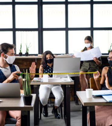 Business people with face masks indoors in office, coronavirus and safe distance concept.