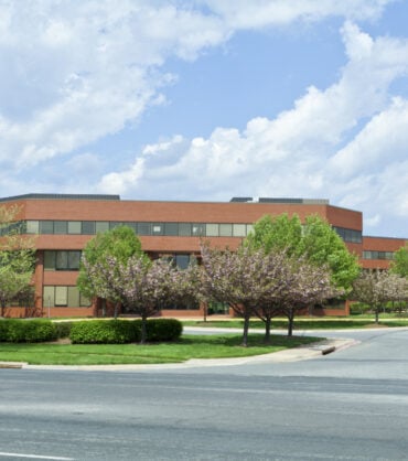 Sprawling red brick office building in suburban Maryland, United States.  Building is set back from the road, and has low trees in front.