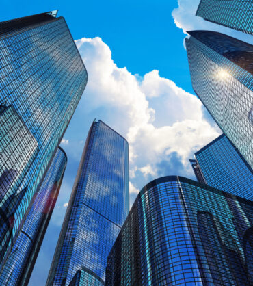 Downtown corporate business district architecture: glass reflective office buildings skyscrapers against blue sky with clouds and sun light