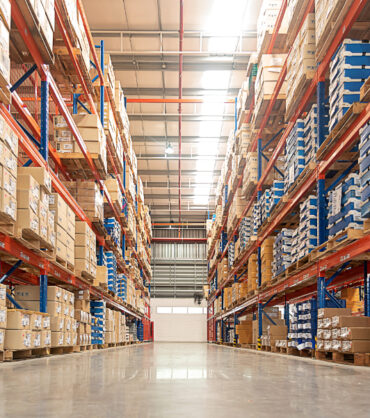 Rows of shelves with goods boxes in huge distribution 
warehouse at industrial storage factory.